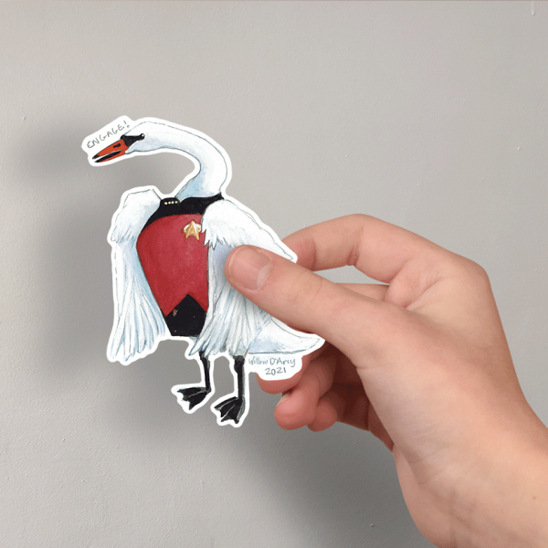 Photo of a hand holding a sticker of an illustration of a swan wearing a science fiction character costume and saying "Engage!"