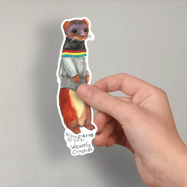 Photo of a hand holding a sticker of an illustration of a weasel wearing a science fiction character costume.