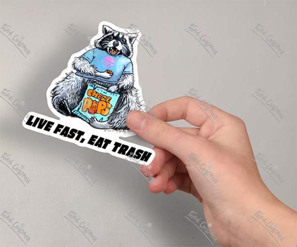 A sticker of an illustration of a raccoon wearing a tee-shirt eating from a bag of chips with the caption “Live Fast, Eat Trash.”